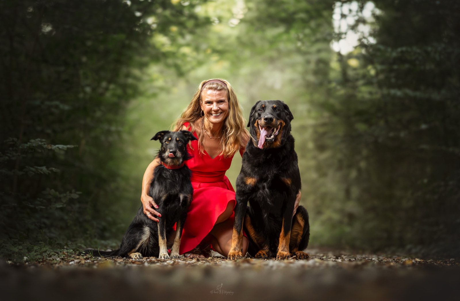 Verena Berg sitzt lächelnd im Wald mit ihren beiden Hunden